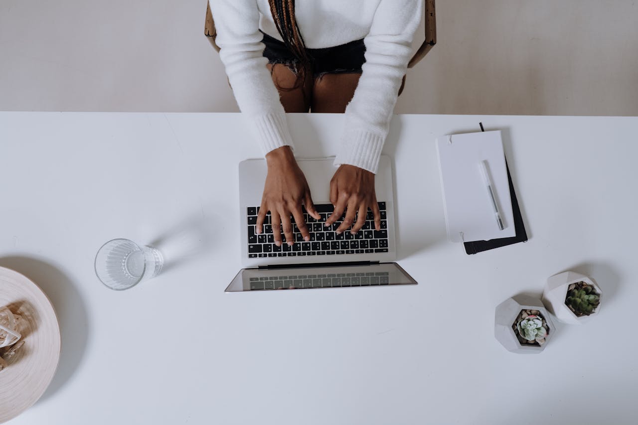 why-choose-us-01 Top view of a woman typing on a laptop at a modern, minimalist home office desk with plants.